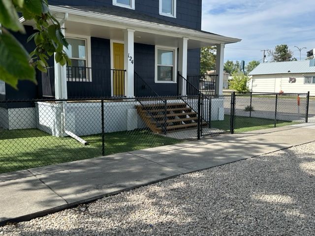 A blue house with a yellow door is behind a chain link fence.