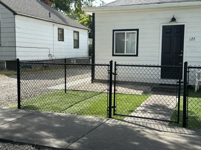 A chain link fence surrounds a white house with a black door.