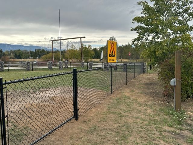 A chain link fence surrounds a field with a sign in the background.