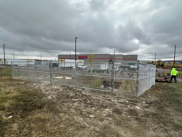 A man in a yellow vest is standing in front of a chain link fence.