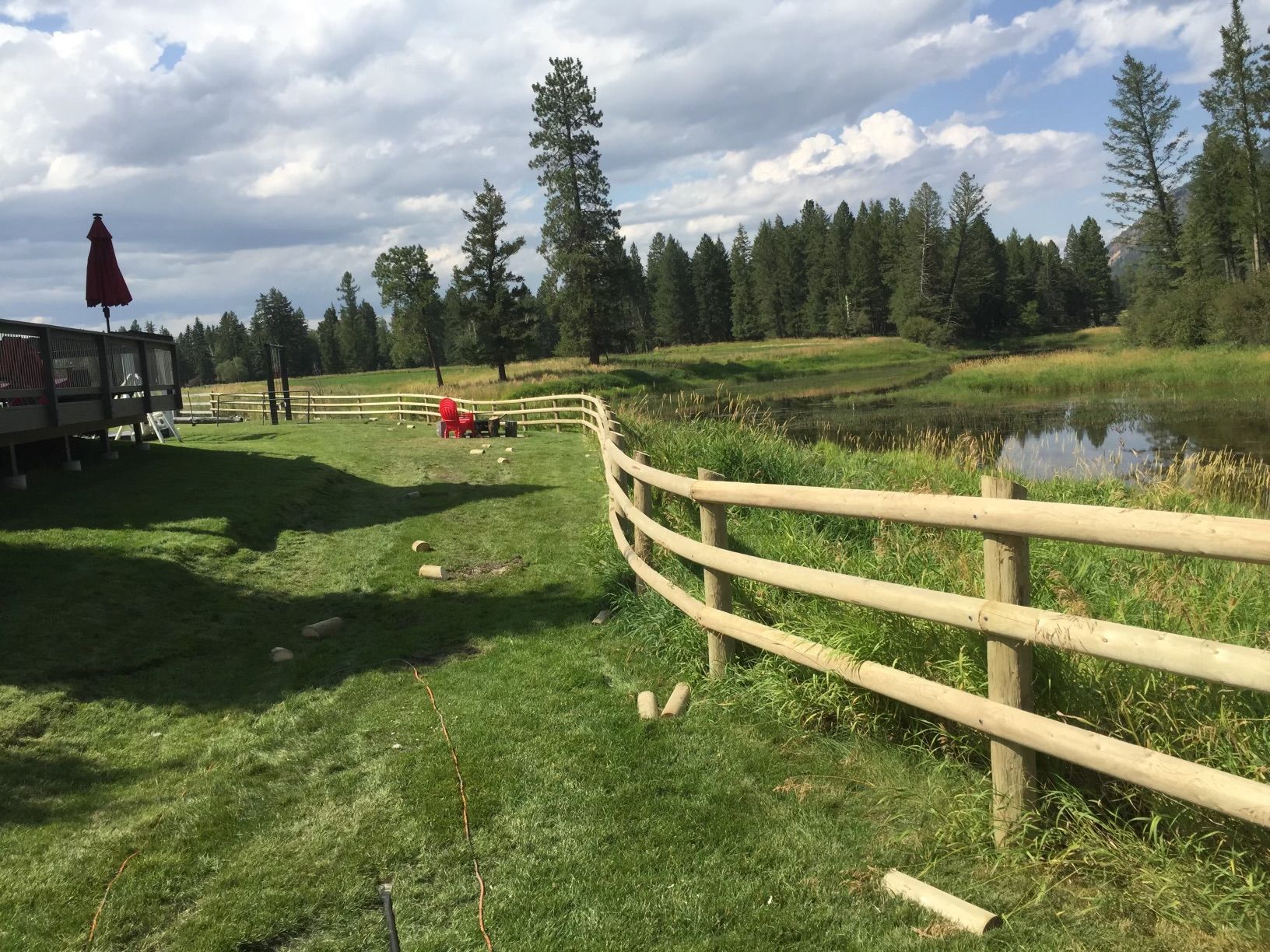 A wooden fence surrounds a grassy field next to a lake.