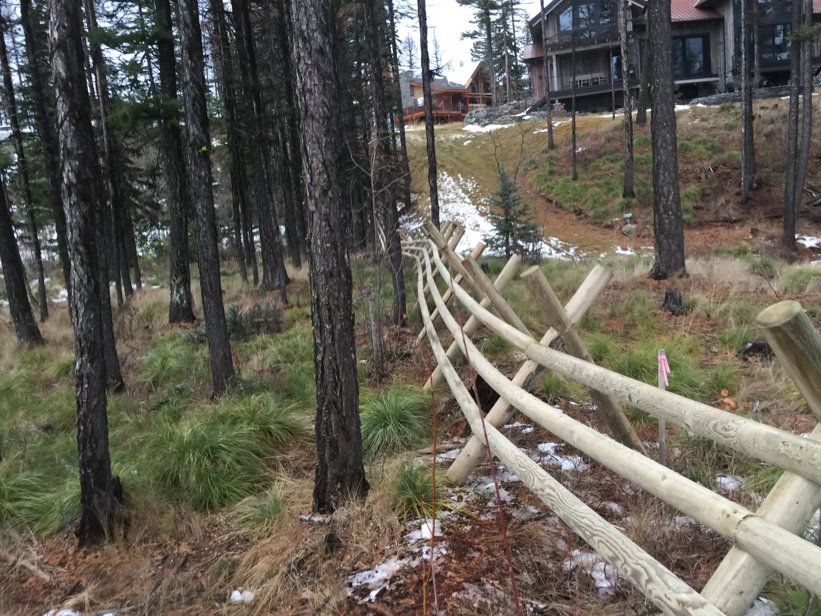A wooden fence in the middle of a forest with a house in the background