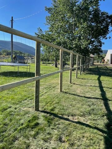 A wooden fence surrounds a lush green field.