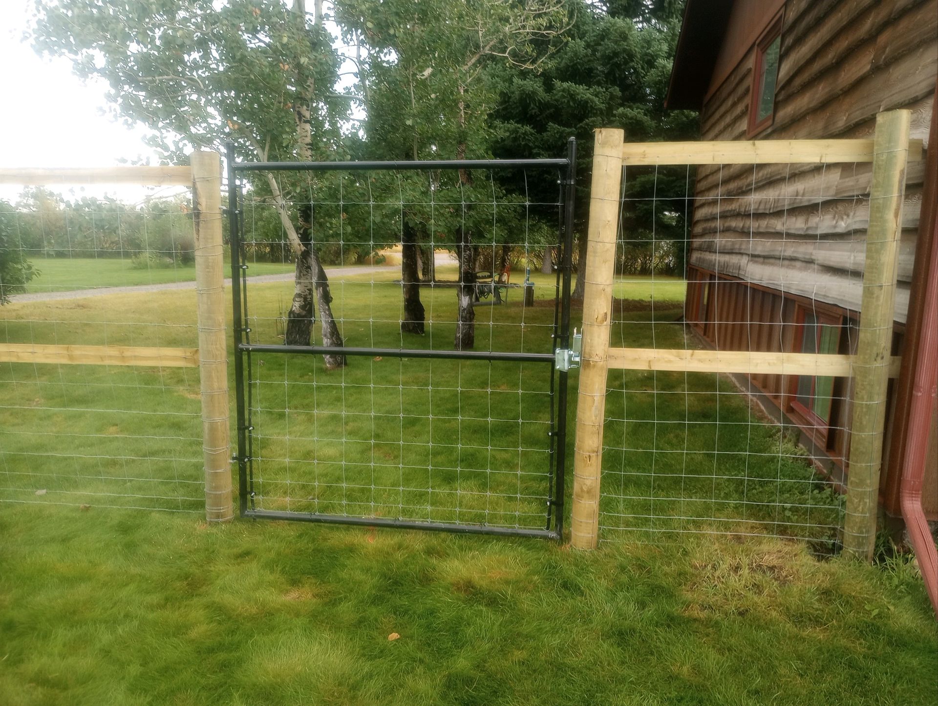 A wooden fence with a metal gate in front of a house.