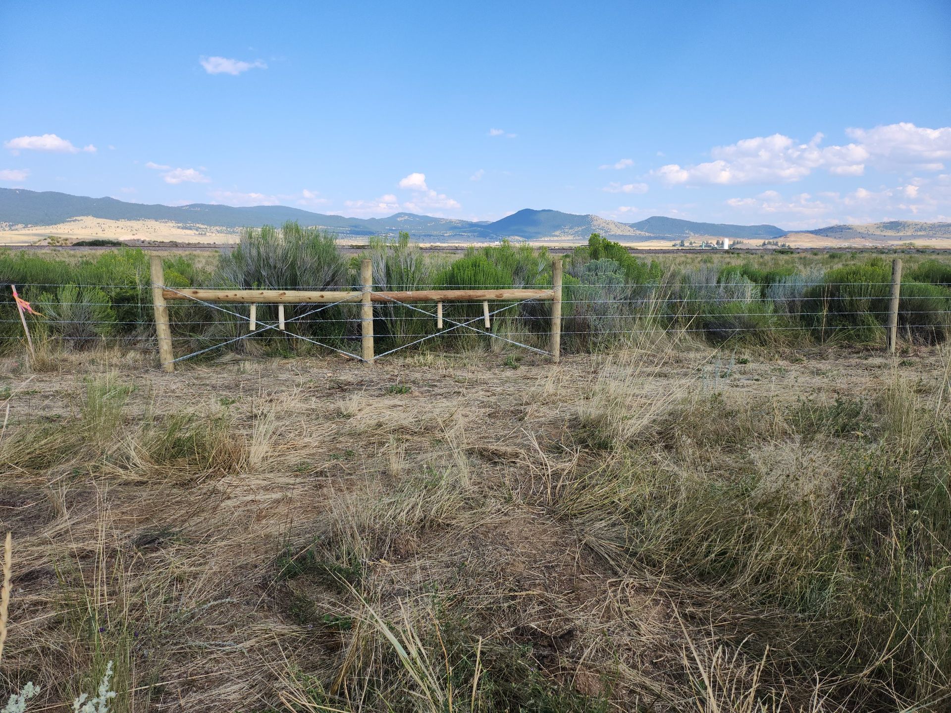 There is a fence in the middle of a field with mountains in the background.