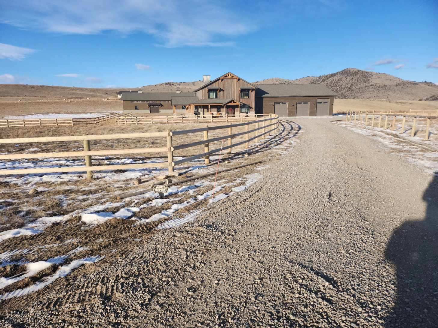 A gravel road leading to a house with mountains in the background