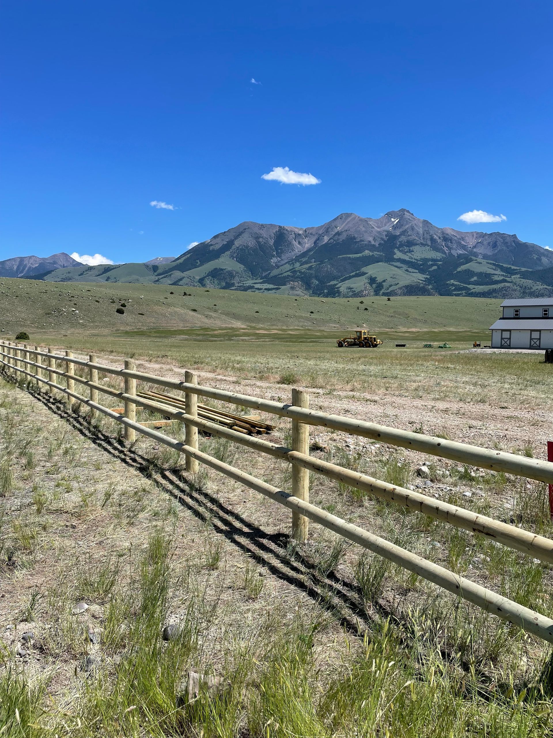A wooden fence surrounds a field with mountains in the background.