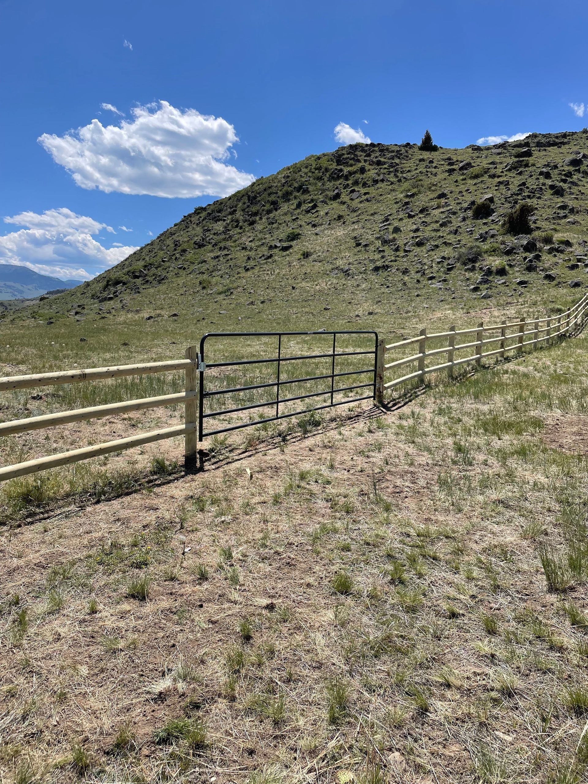 A wooden fence with a gate in the middle of a field with a mountain in the background.