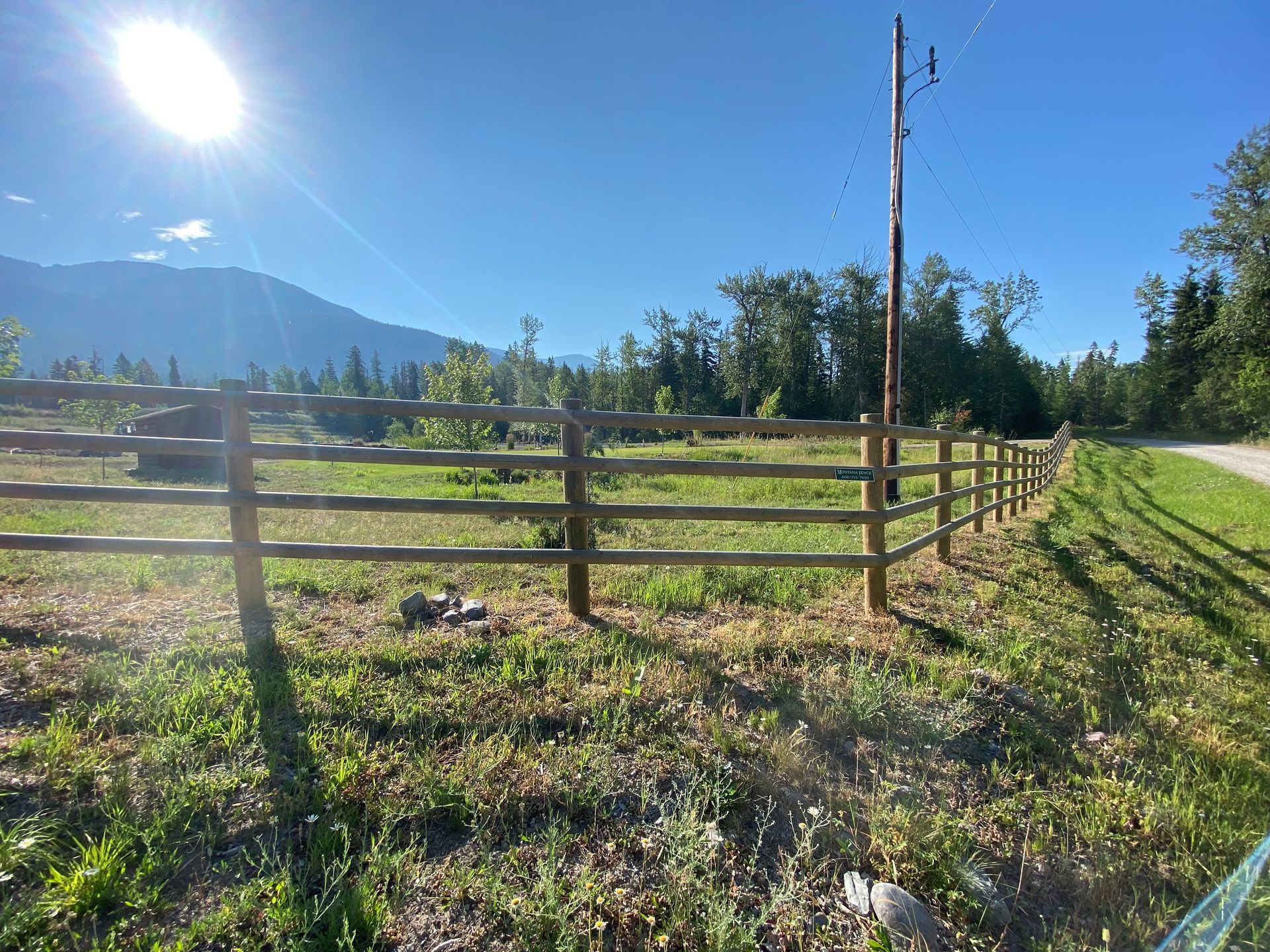 A wooden fence surrounds a grassy field with mountains in the background.
