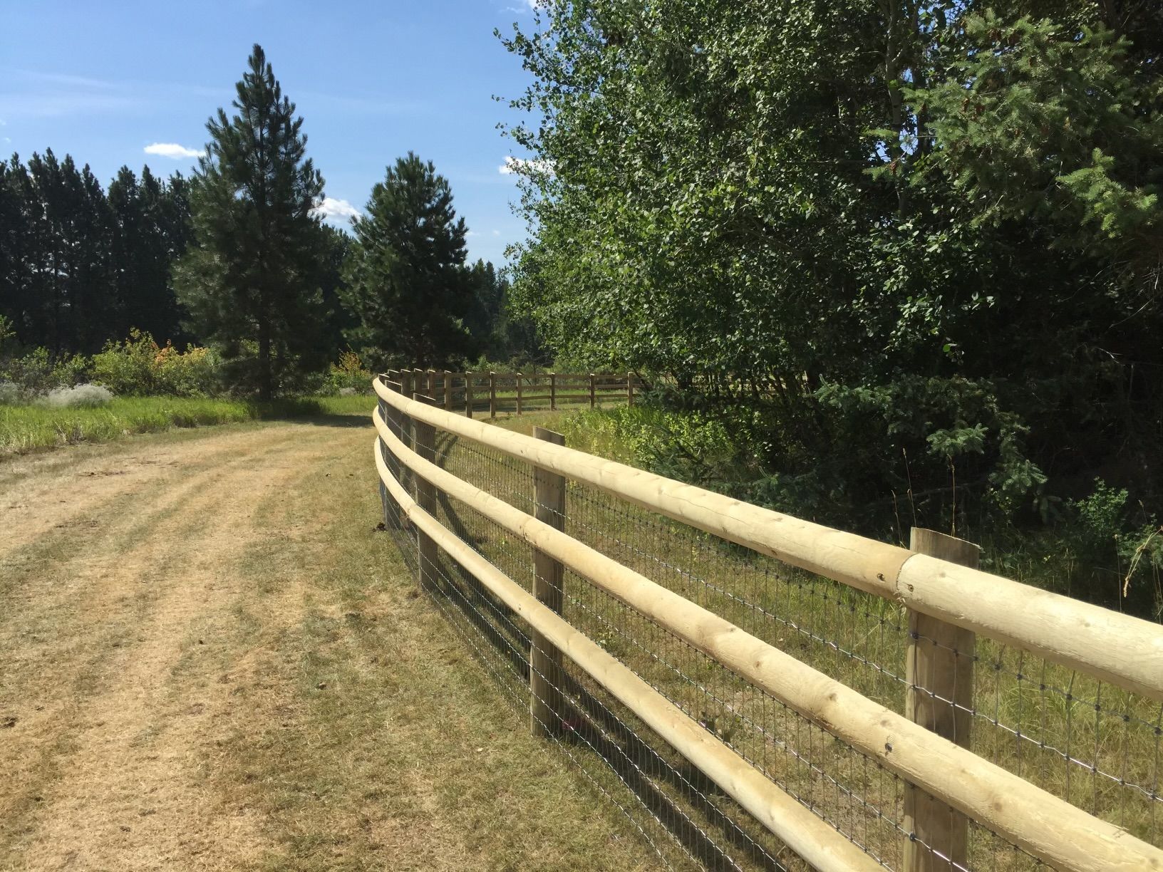 A wooden fence along a dirt road with trees in the background