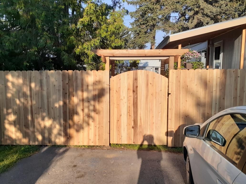 A car is parked in front of a wooden fence and gate.