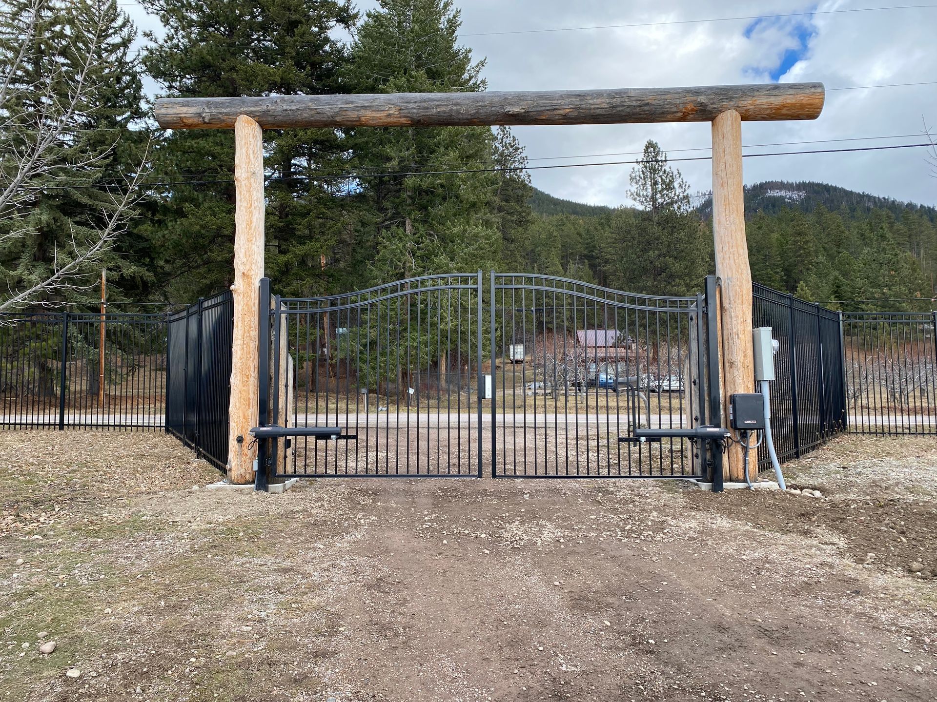 A metal gate with a wooden post in the middle of a dirt field.