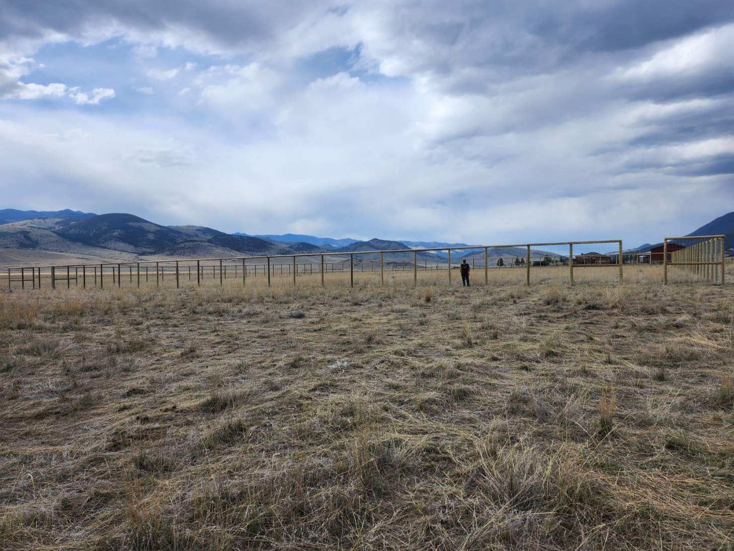 A fenced in field with mountains in the background on a cloudy day.