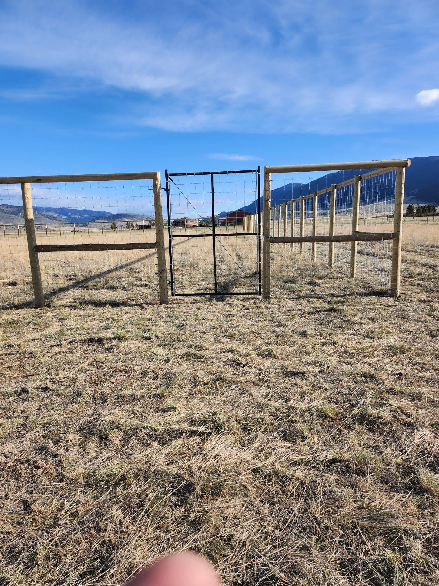 A person is standing in a field with a fence and a gate.