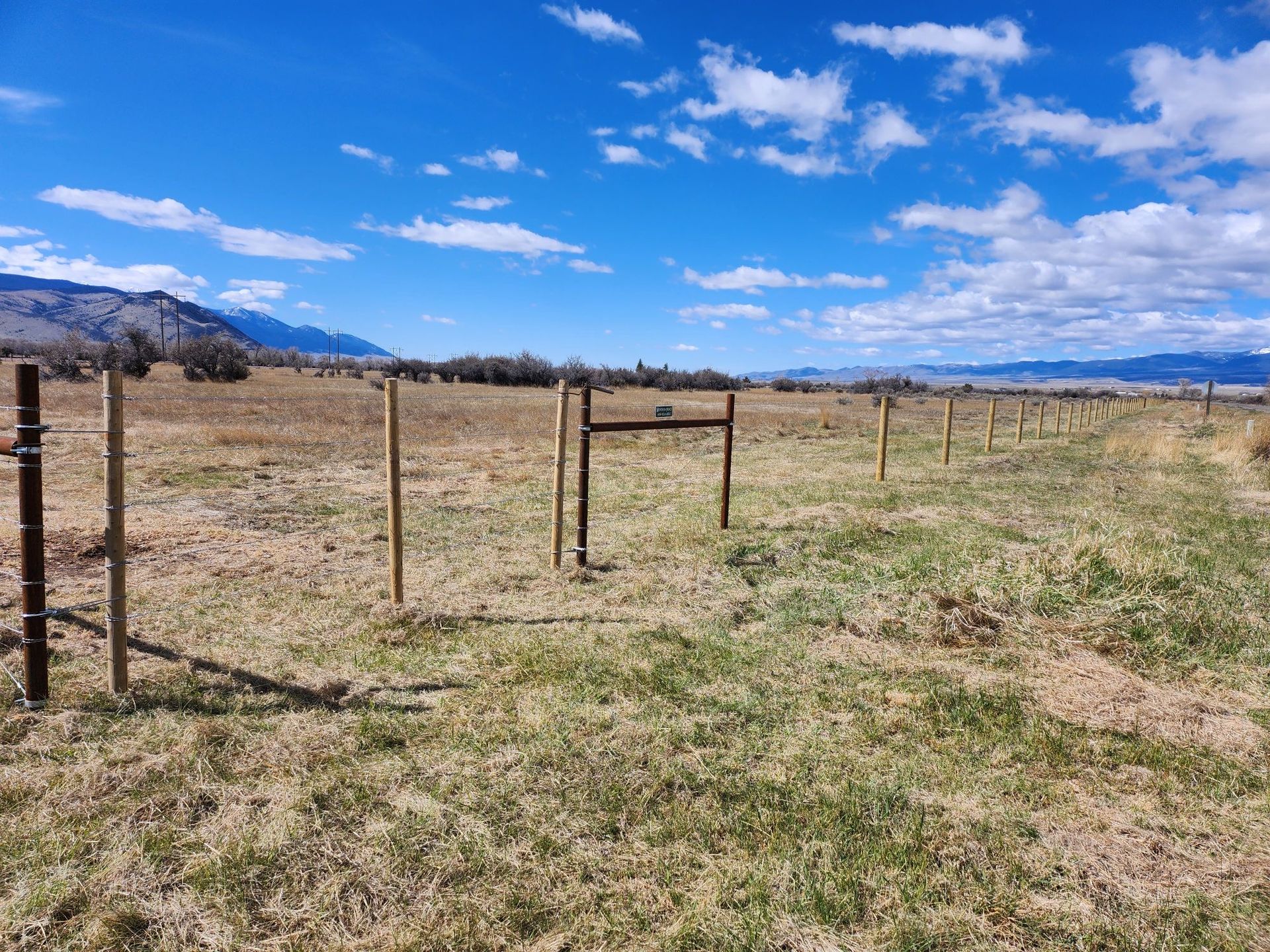 A fence surrounds a grassy field with mountains in the background.