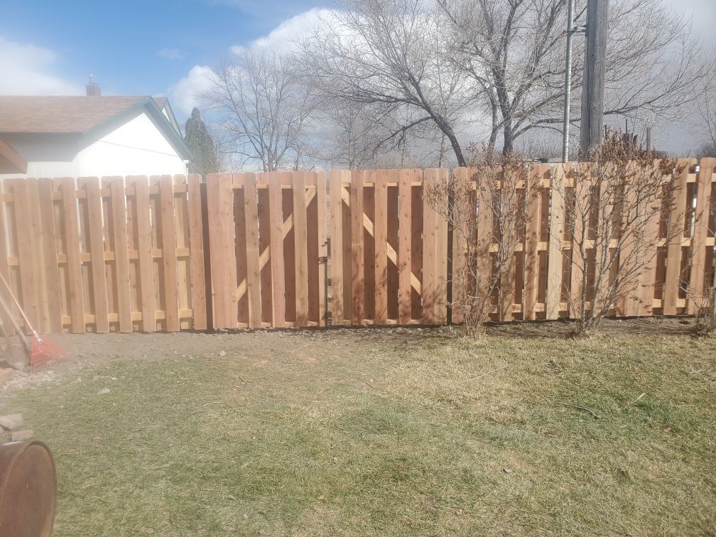 A wooden fence in a backyard with a house in the background.