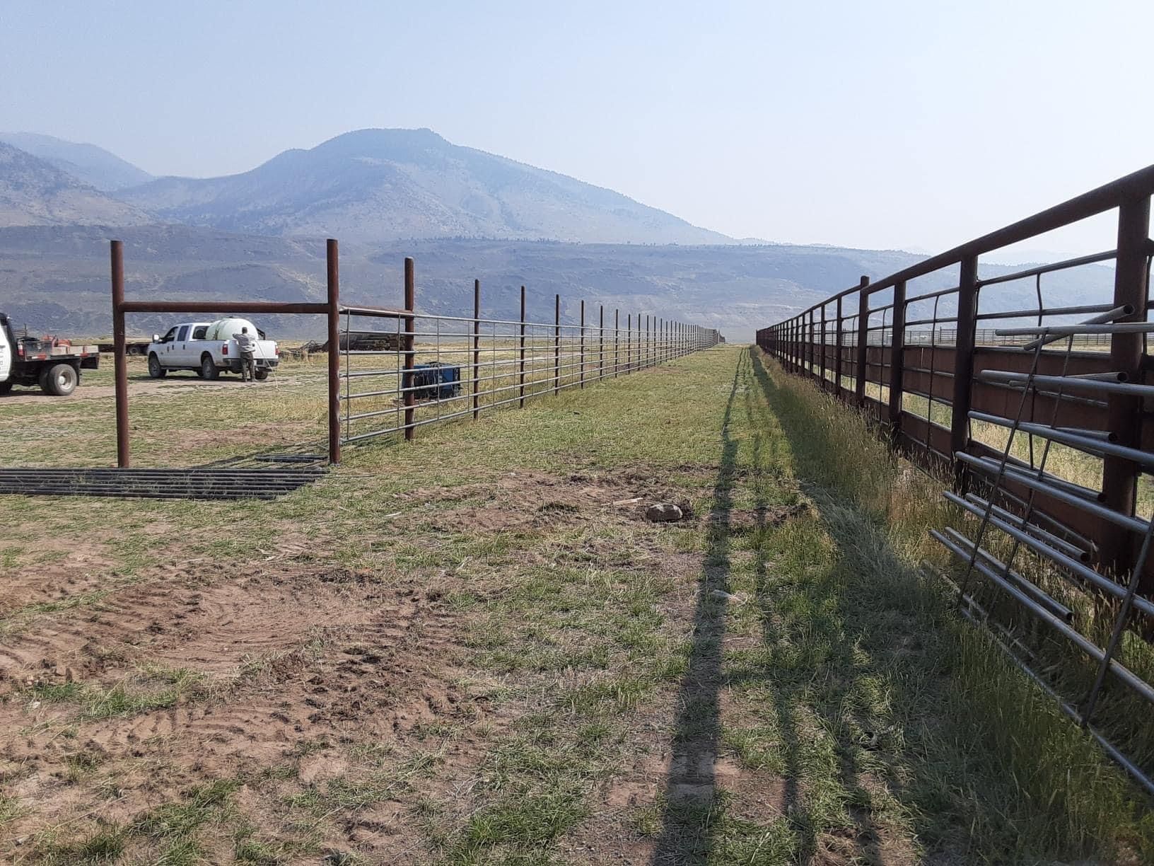 A fence is being built in a field with mountains in the background.