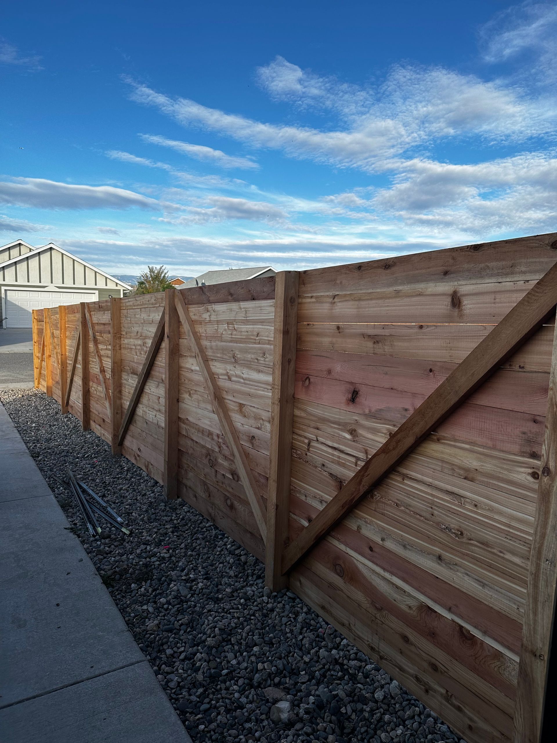 A wooden fence is sitting next to a sidewalk in front of a house.