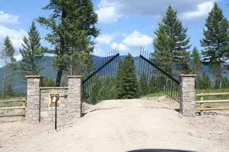 A gate leading to a dirt road surrounded by trees and mountains.
