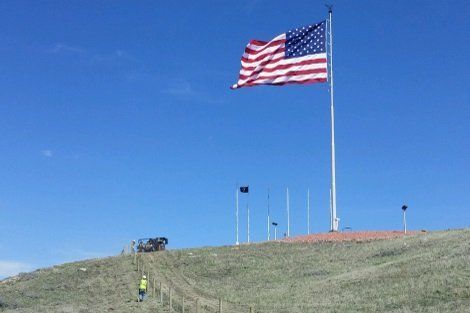 A large american flag is flying in the wind on top of a hill
