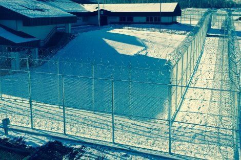 A barbed wire fence surrounds a building in the snow.