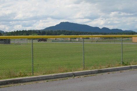 A chain link fence surrounds a baseball field with mountains in the background