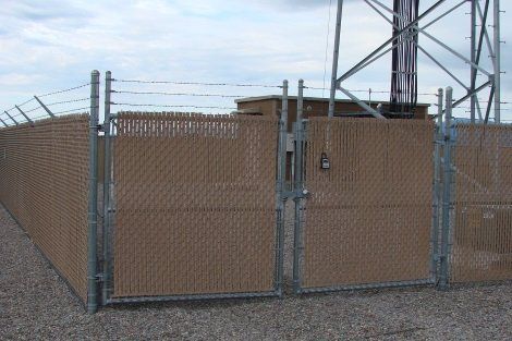 A chain link fence with a gate and a tower in the background.