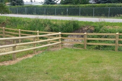 A wooden fence surrounds a lush green field.