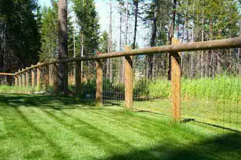 A wooden fence surrounds a lush green field.
