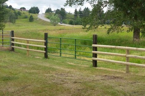 A wooden fence with a gate in the middle of a grassy field.