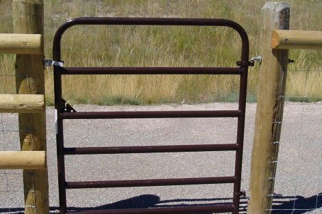 A brown metal gate is next to a wooden fence