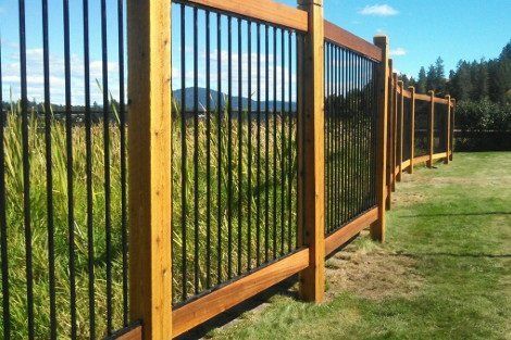 A wooden fence with black metal bars surrounding a grassy field.