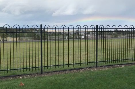 There is a rainbow in the sky behind the fence.