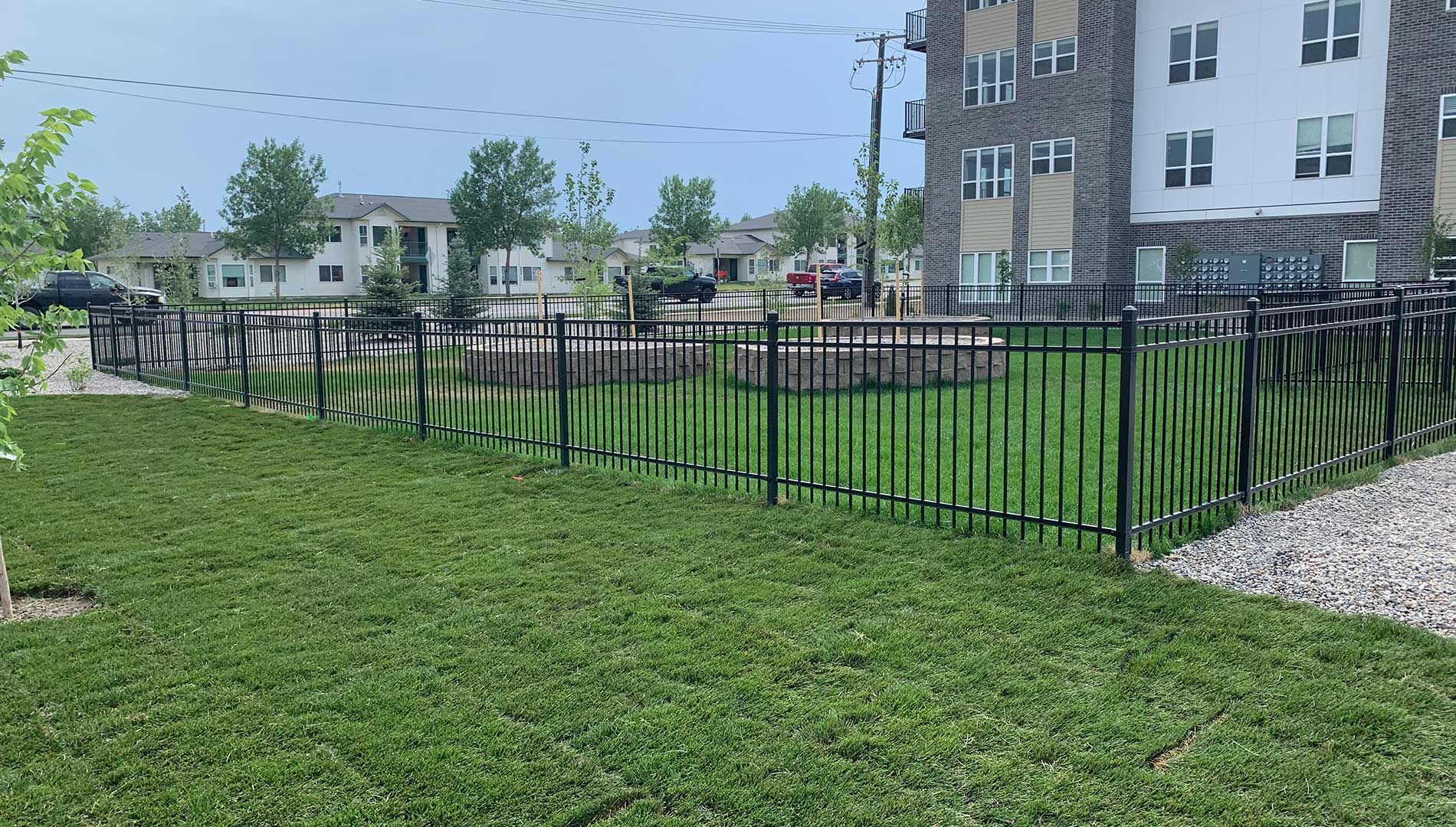A black metal fence surrounds a lush green lawn in front of a building.