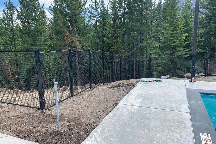 A fence surrounds a swimming pool with trees in the background.
