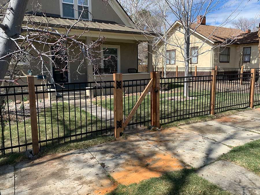 A metal fence with wooden posts is in front of a house.