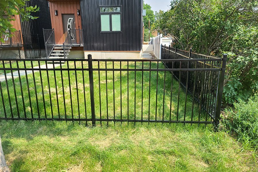 A black fence surrounds a lush green yard in front of a house.