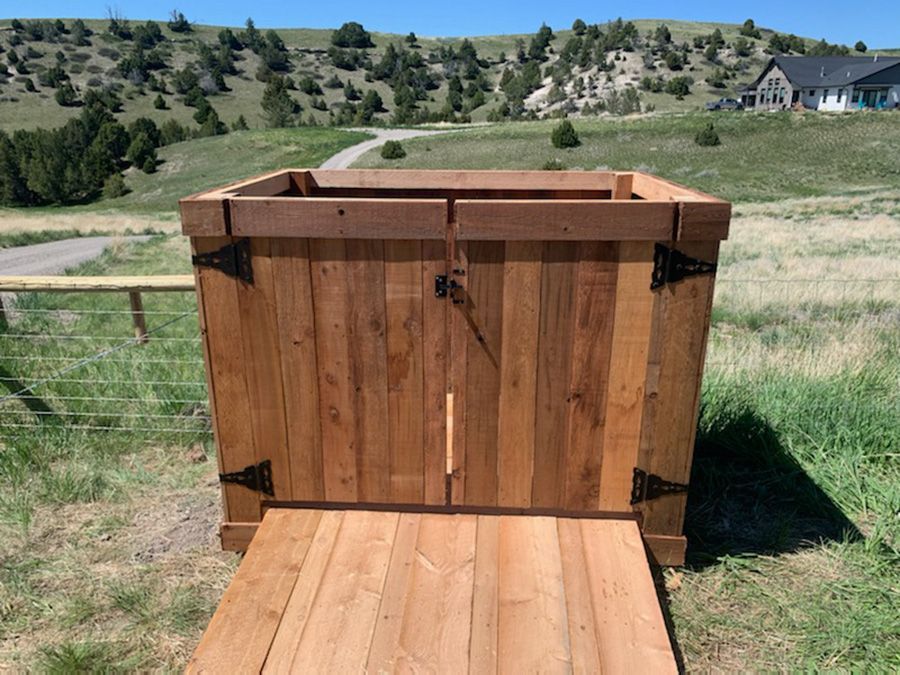 A wooden box is sitting on top of a wooden deck in a grassy field.