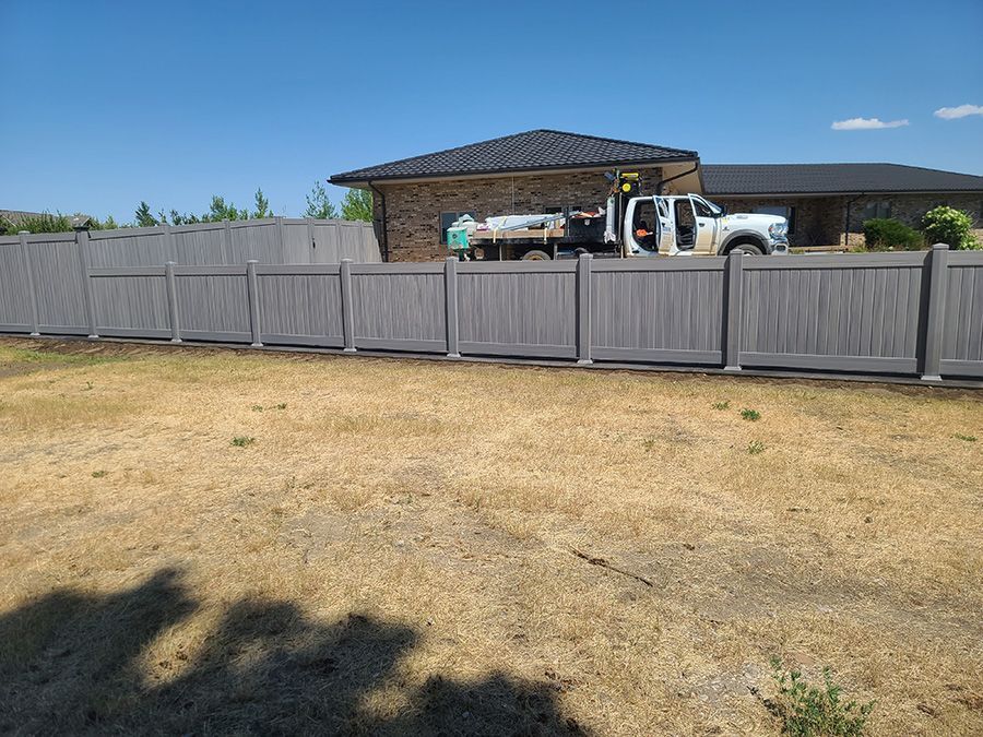 A truck is parked behind a wooden fence in front of a house.