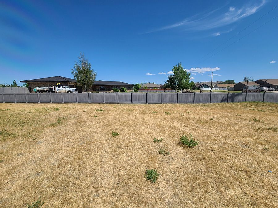 A fence surrounds a dry grassy field with a house in the background.