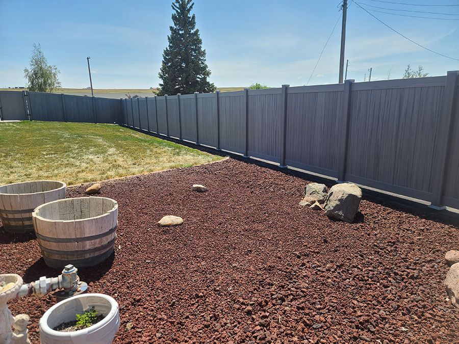 A backyard with a fence and potted plants and rocks.
