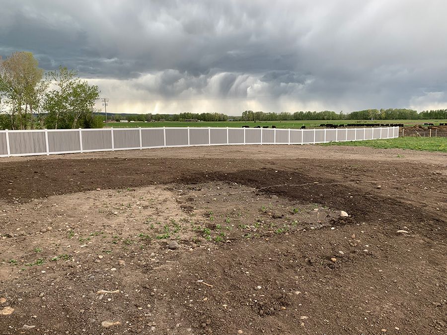 A white fence surrounds a dirt field with a cloudy sky in the background.