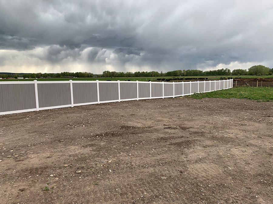 A white fence surrounds a dirt field with a cloudy sky in the background.