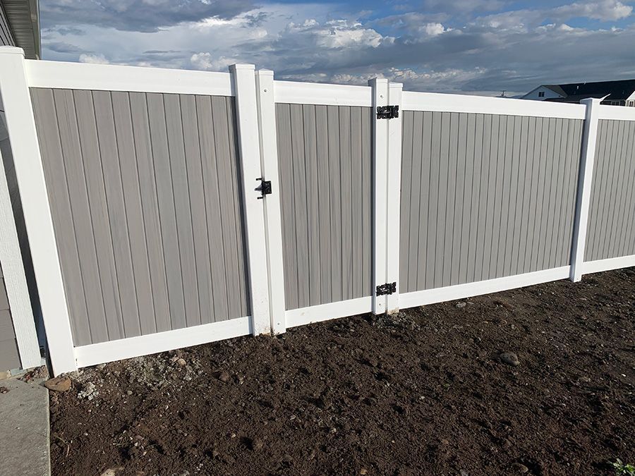 A white and gray fence with a gate is sitting on top of a pile of dirt.