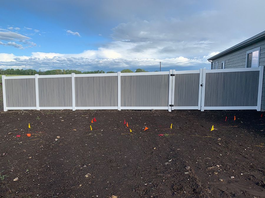 A white fence is sitting in the middle of a dirt field next to a house.