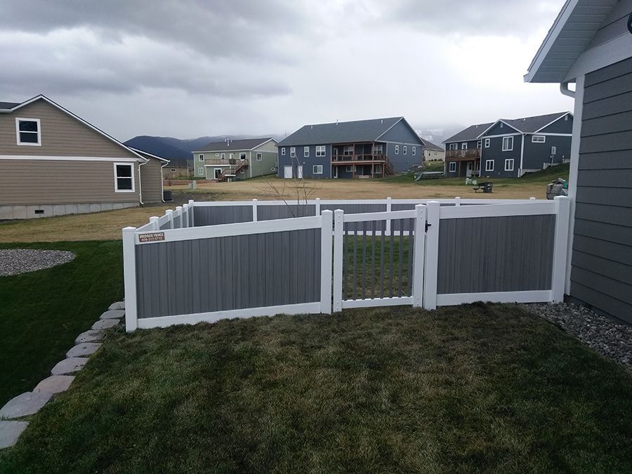 A gray and white fence is in the backyard of a house.