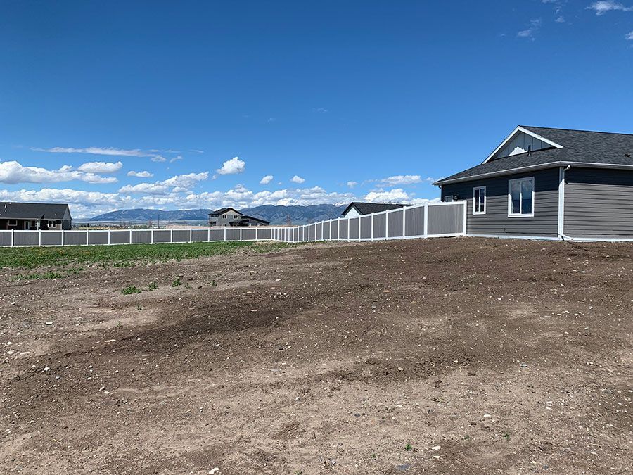 A house is sitting on top of a dirt hill next to a fence.