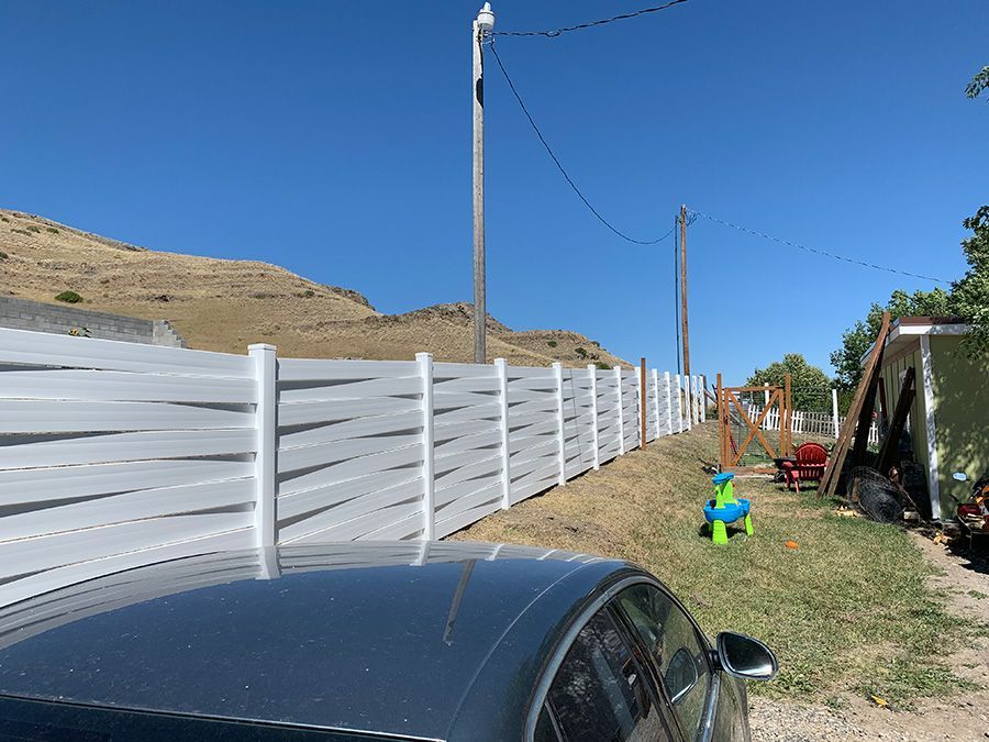 A car is parked in front of a white fence.