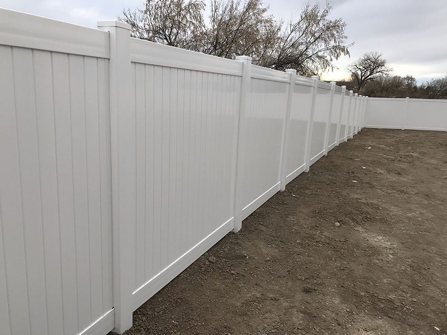 A white vinyl fence is sitting in the middle of a dirt field.