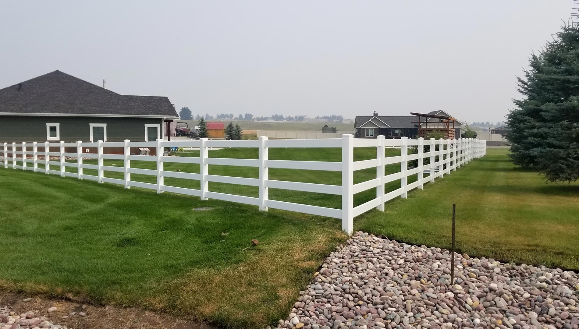 A white fence surrounds a lush green field in front of a house.